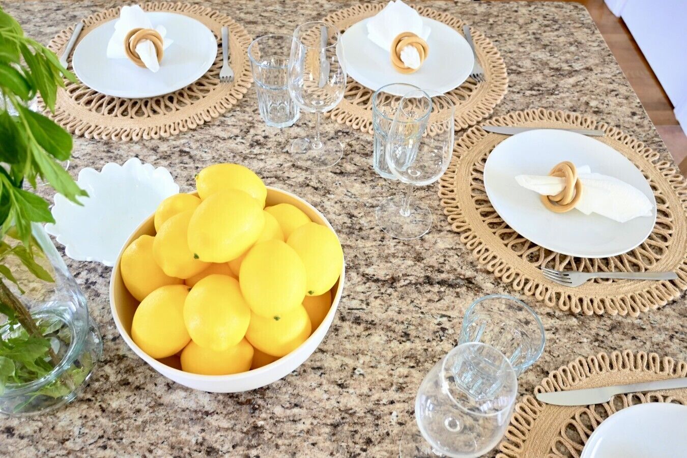 Tavola apparecchiata con piatti, bicchieri e una ciotola di limoni.