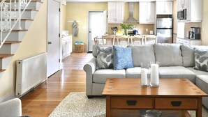 Een woonkamer met een bank, salontafel en een eetgedeelte met stoelen en een tafel.
