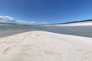 A beach with footprints leading to the water, a clear sky, and a distant shoreline.