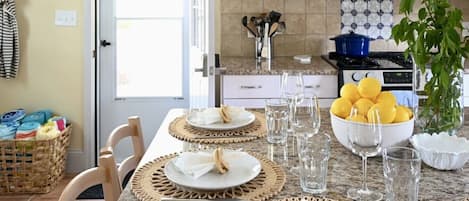A kitchen with a dining table set for four, a bowl of lemons, and a potted plant.