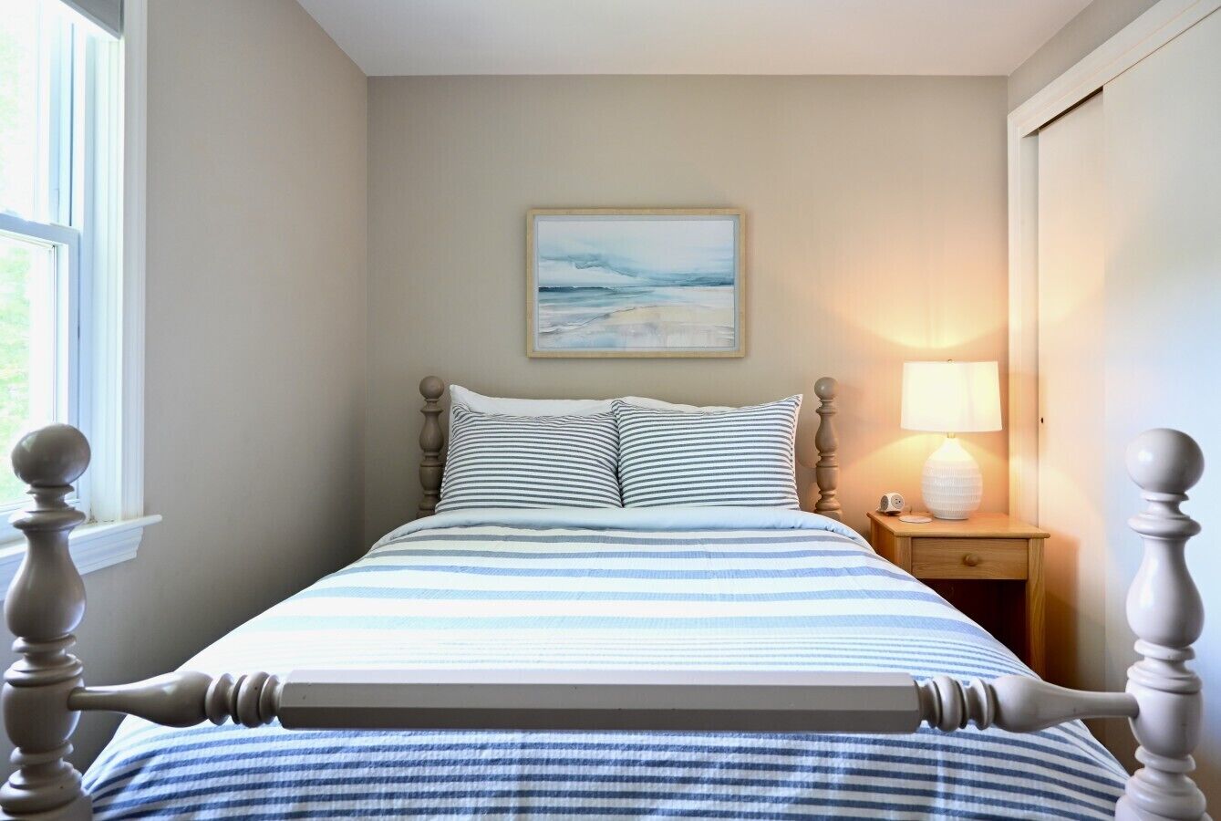 A bed with a headboard, a bedside table with a lamp, and a painting on the wall.