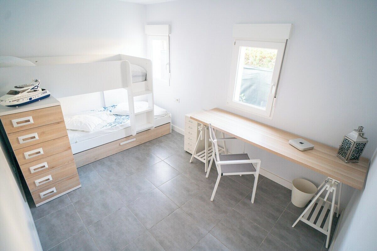 A child's bunk bed with a desk and chair, a small window, and a toy ship on the dresser.