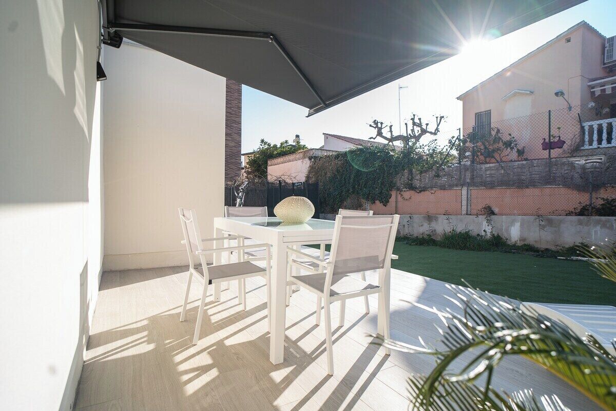 Une terrasse extérieure avec une table et des chaises blanches, une table à plateau en verre et un bol décoratif.