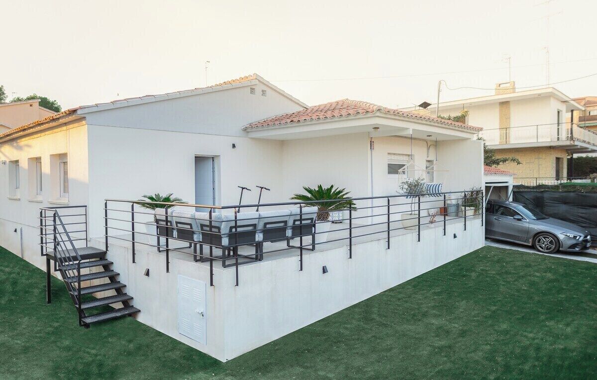 Ein modernes Haus mit weißer Fassade, einem Ziegeldach und einem kleinen Balkon mit Sitzgelegenheit.