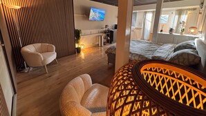 Een moderne woonkamer met een bank, een fauteuil, een televisie en een decoratieve lamp.