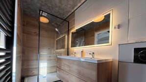 Een moderne badkamer met een douchecabine van glas, een houten wastafelmeubel met een spiegel en een inbouw wasmachine.