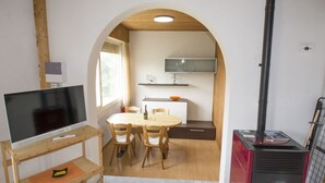 Un espace de vie compact comprenant un téléviseur posé sur un meuble en bois, une table à manger avec des chaises, un coin cuisine avec une cuisinière et un téléviseur fixé au mur.