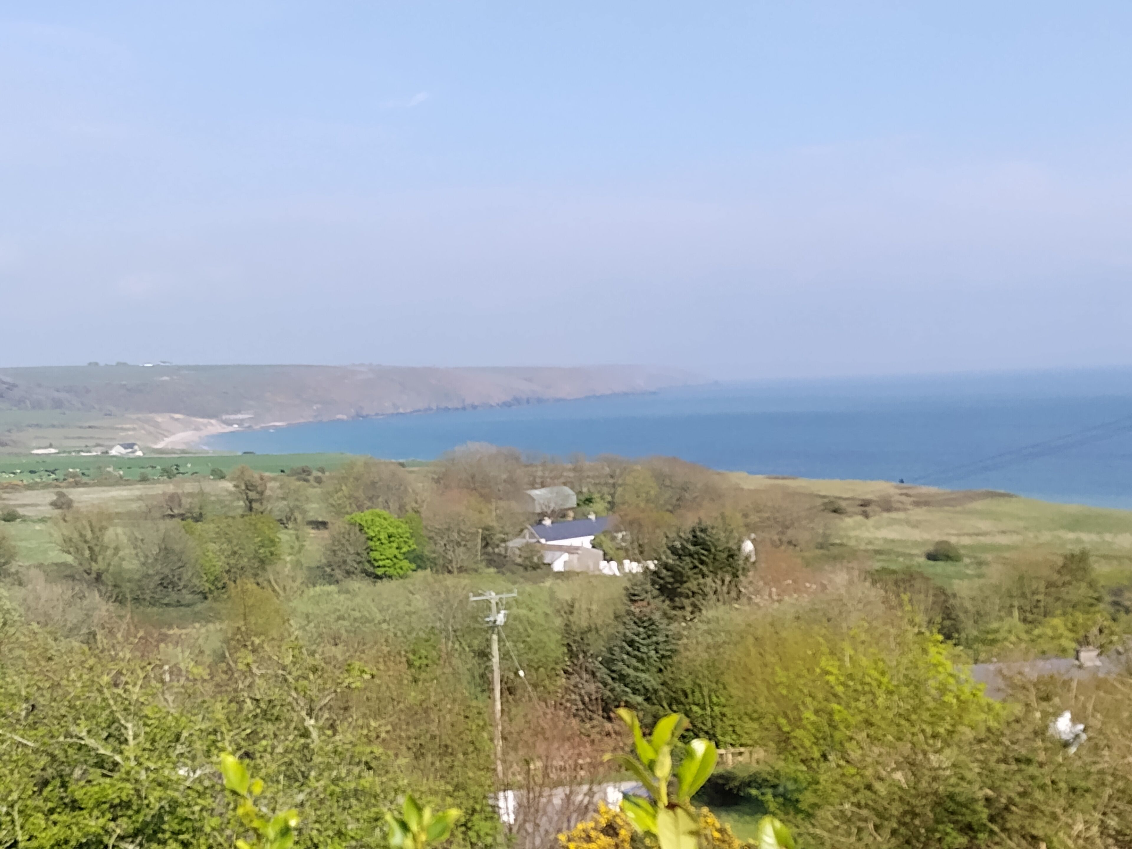 A coastal landscape with a view of the sea, rolling hills, and scattered houses.