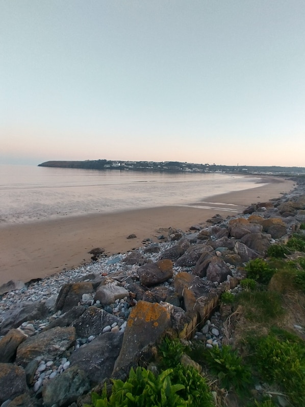 Un paisaje costero con una playa de arena, un litoral rocoso y una vista distante de un pueblo.