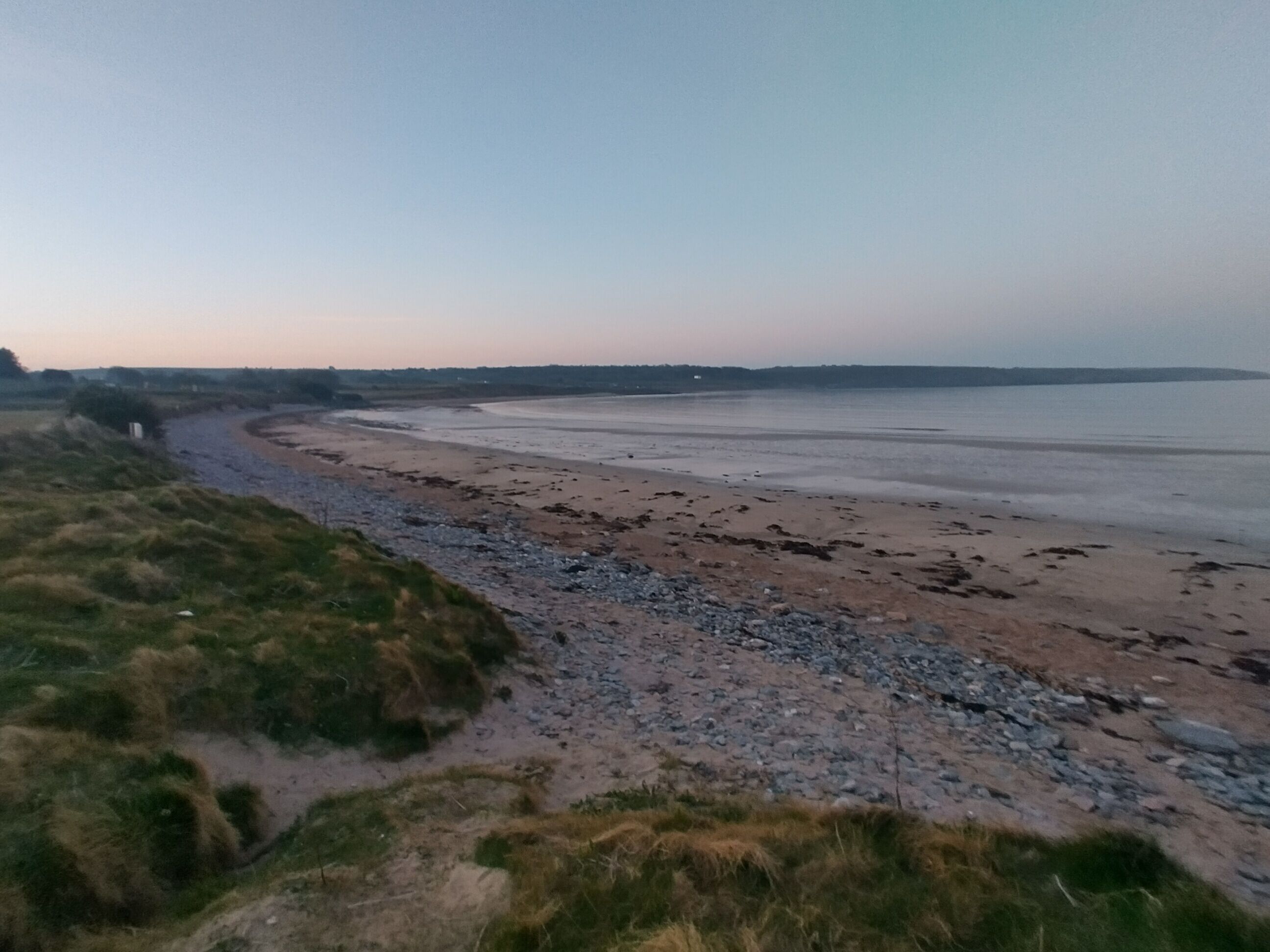 A coastal landscape with a sandy beach, rocky shoreline, and grassy dunes.