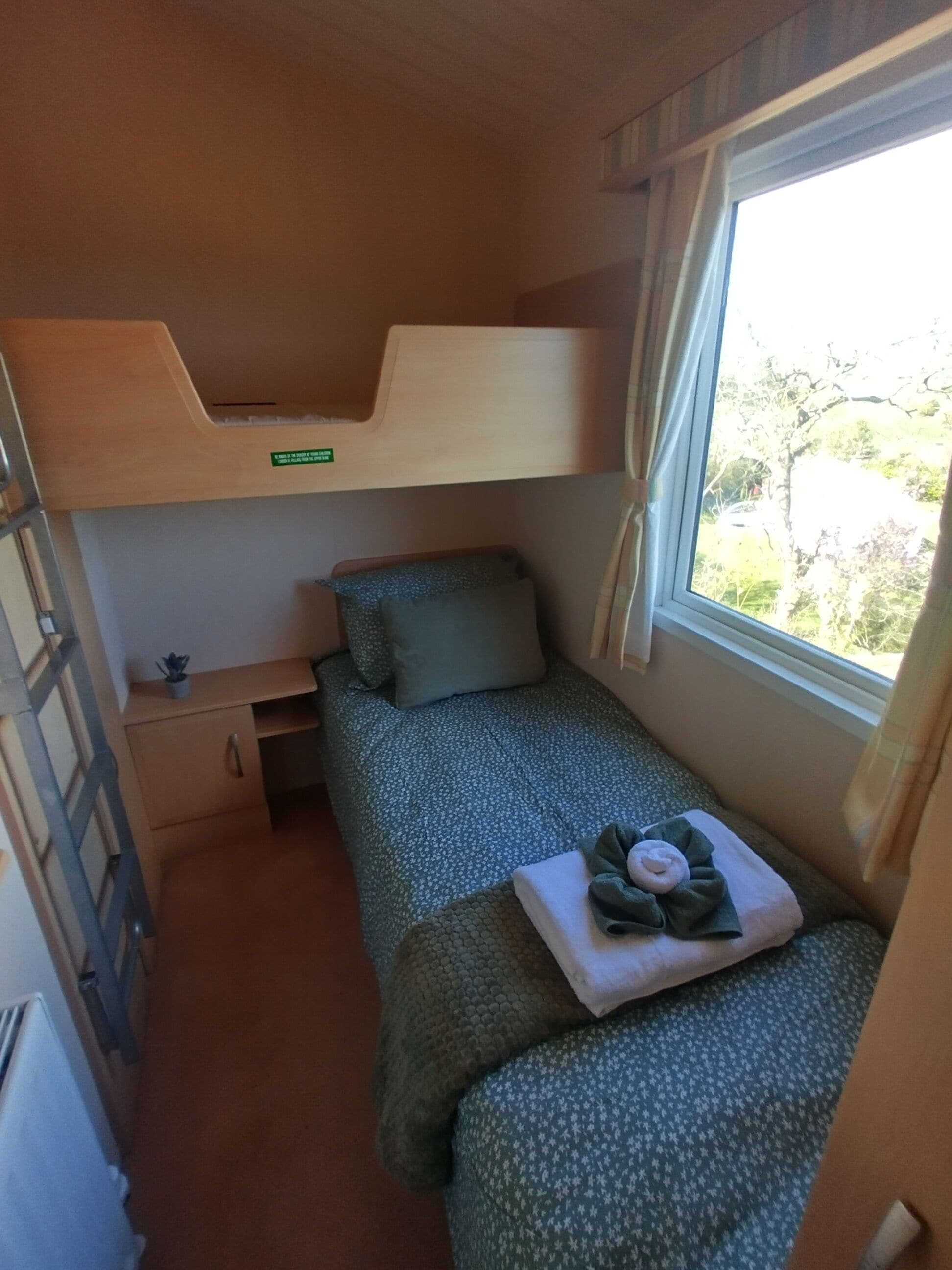 Una camera compatta con un letto a castello, una piccola scrivania e una finestra vista verde.