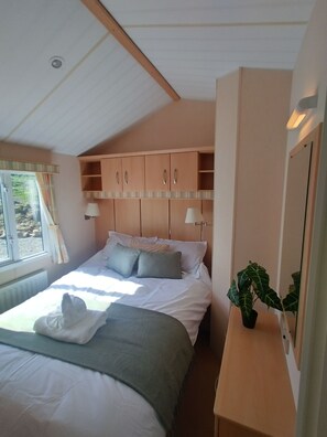 Un dormitorio con una cama, una mesita de noche, una planta en maceta y una ventana con cortinas.