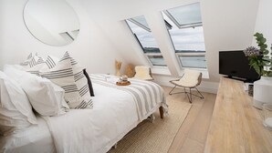 A modern bedroom with a bed, a TV, and a view of the water. - Cornwall Beachfront Stay | Walk to Pubs & Pasties (Cawsand)