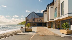A coastal property with a wooden building labeled "The Bay," featuring a paved driveway and potted plants. - Cornwall Beachfront Stay | Walk to Pubs & Pasties (Cawsand)