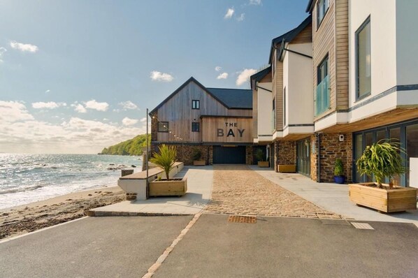 A coastal property with a wooden building labeled "The Bay," featuring a paved driveway and potted plants.