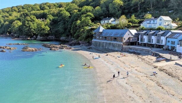 A coastal hotel with a beach, kayaks, and people on the shore. - Cornwall Beachfront Stay | Walk to Pubs & Pasties (Cawsand)
