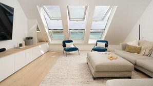 A modern loft bedroom with skylights, a sofa, a TV, and a view of the sea. - Cornwall Beachfront Stay | Walk to Pubs & Pasties (Cawsand)