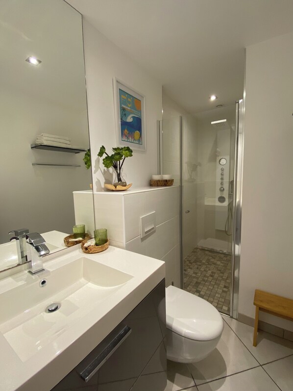 A modern bathroom with a large mirror, a white sink, a toilet, and a glass-enclosed shower.