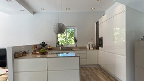 A modern kitchen with white cabinets, a central island, a hanging light fixture, and a window with a view of greenery. - Villa with pool, 15 min walk from the beach (Hendaye)