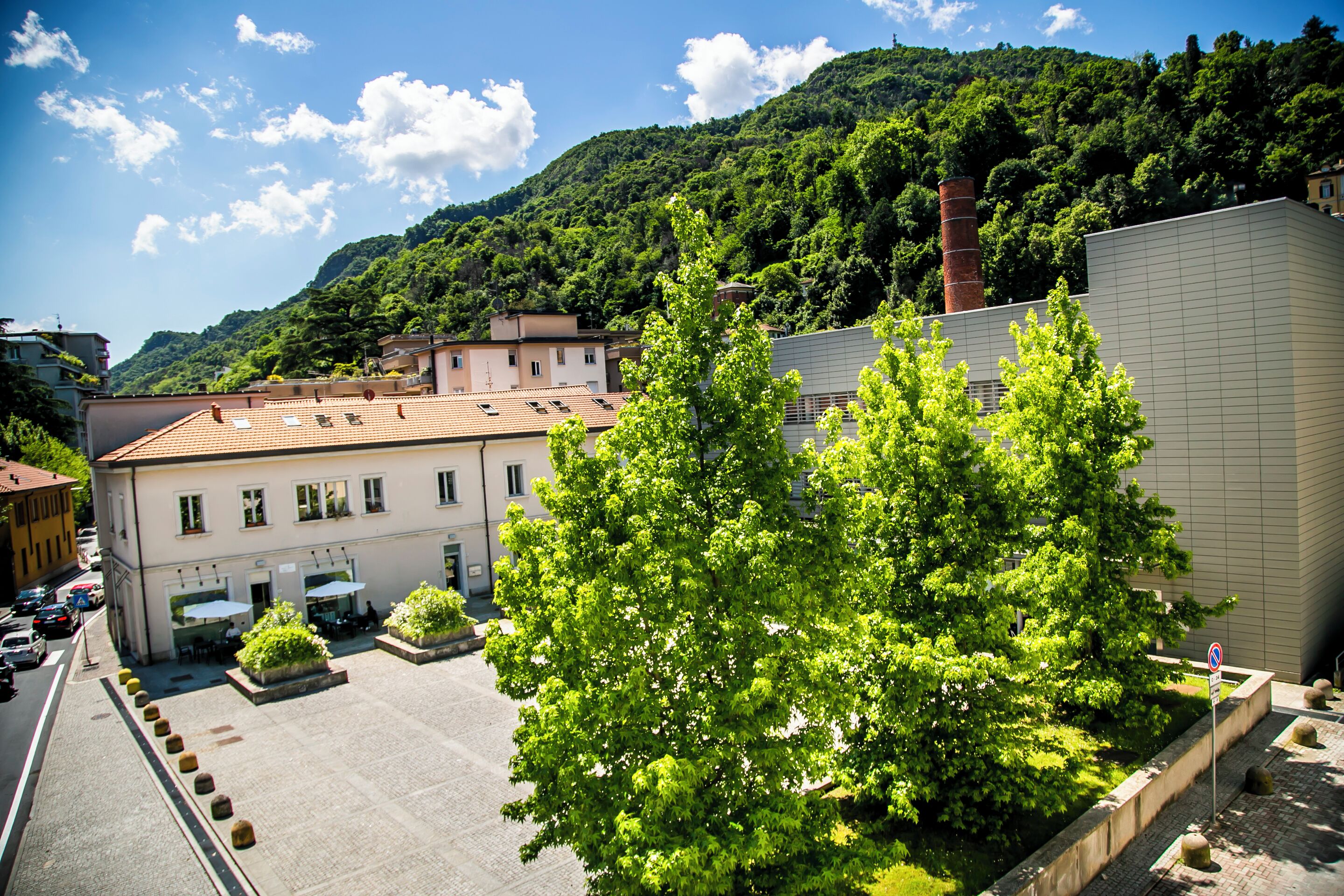 Um edifício com telhado de cerâmica, um pátio com árvores e montanhas ao fundo.