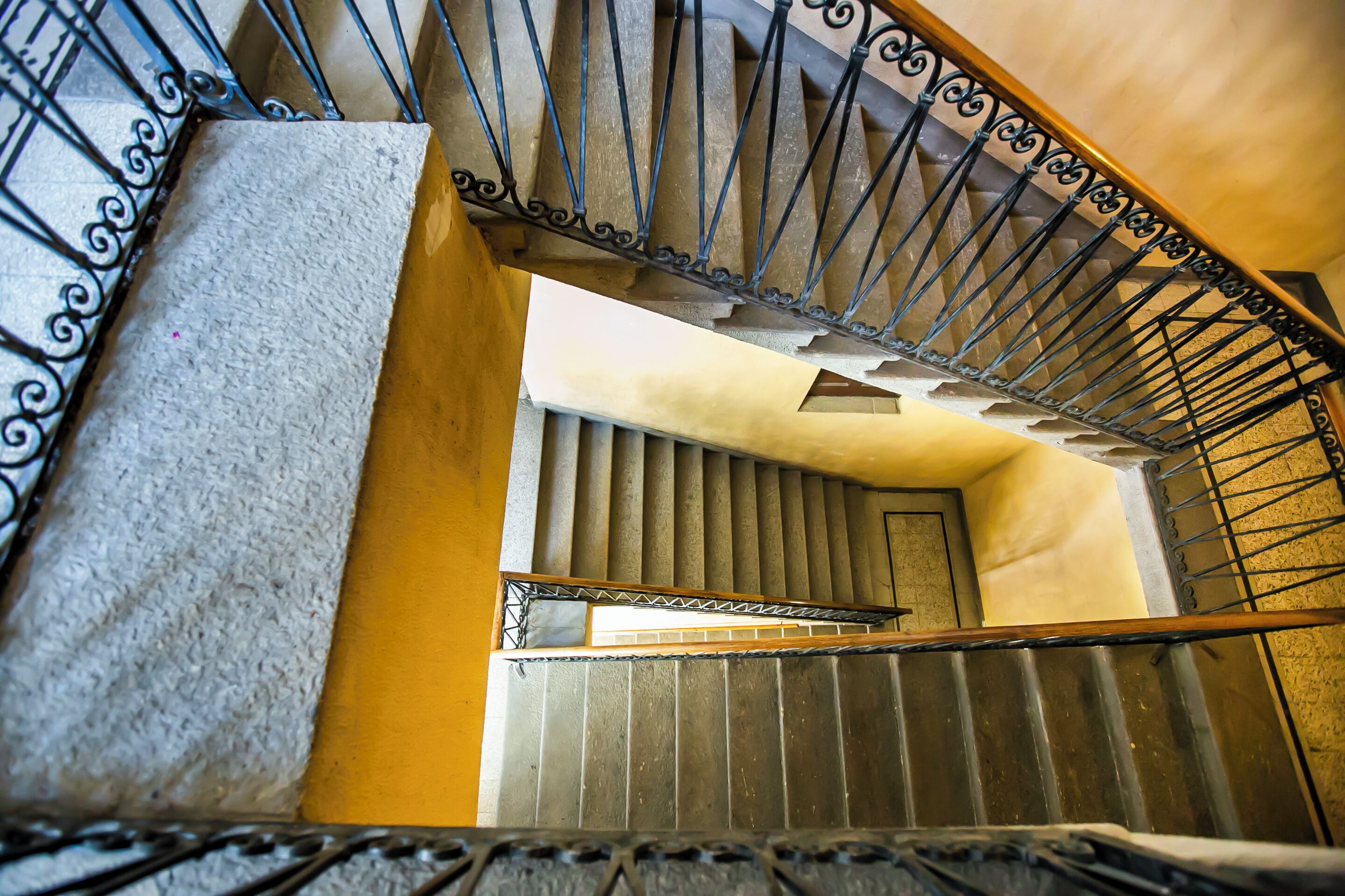 A staircase with a metal railing and a handrail, leading to a door with vertical blinds.