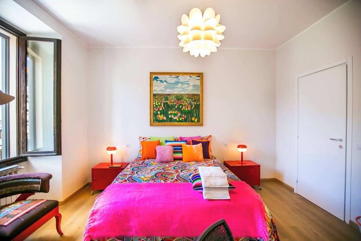Ein Schlafzimmer mit farbenfroher Bettdecke, einem Bild an der Wand und einer modernen Lampenleuchte.
