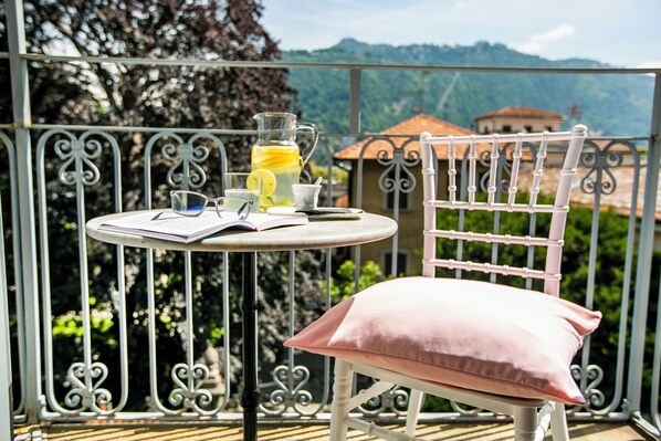 A balcony with a table set for two, a pink cushion, a glass pitcher with a yellow drink, and a book.