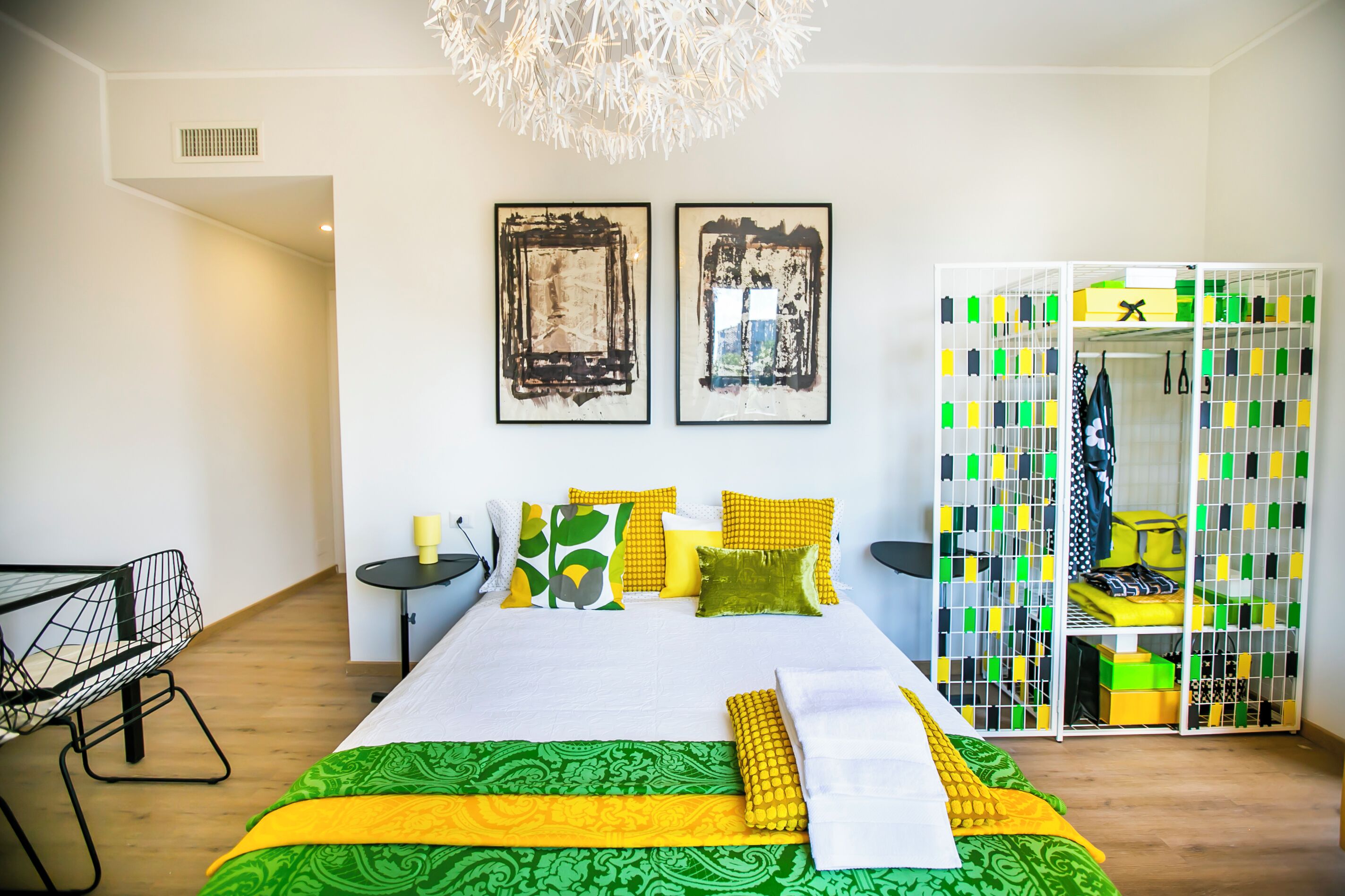 Quarto moderno com uma cama grande, um guarda-roupa com caixas organizadoras e duas pinturas abstratas na parede.