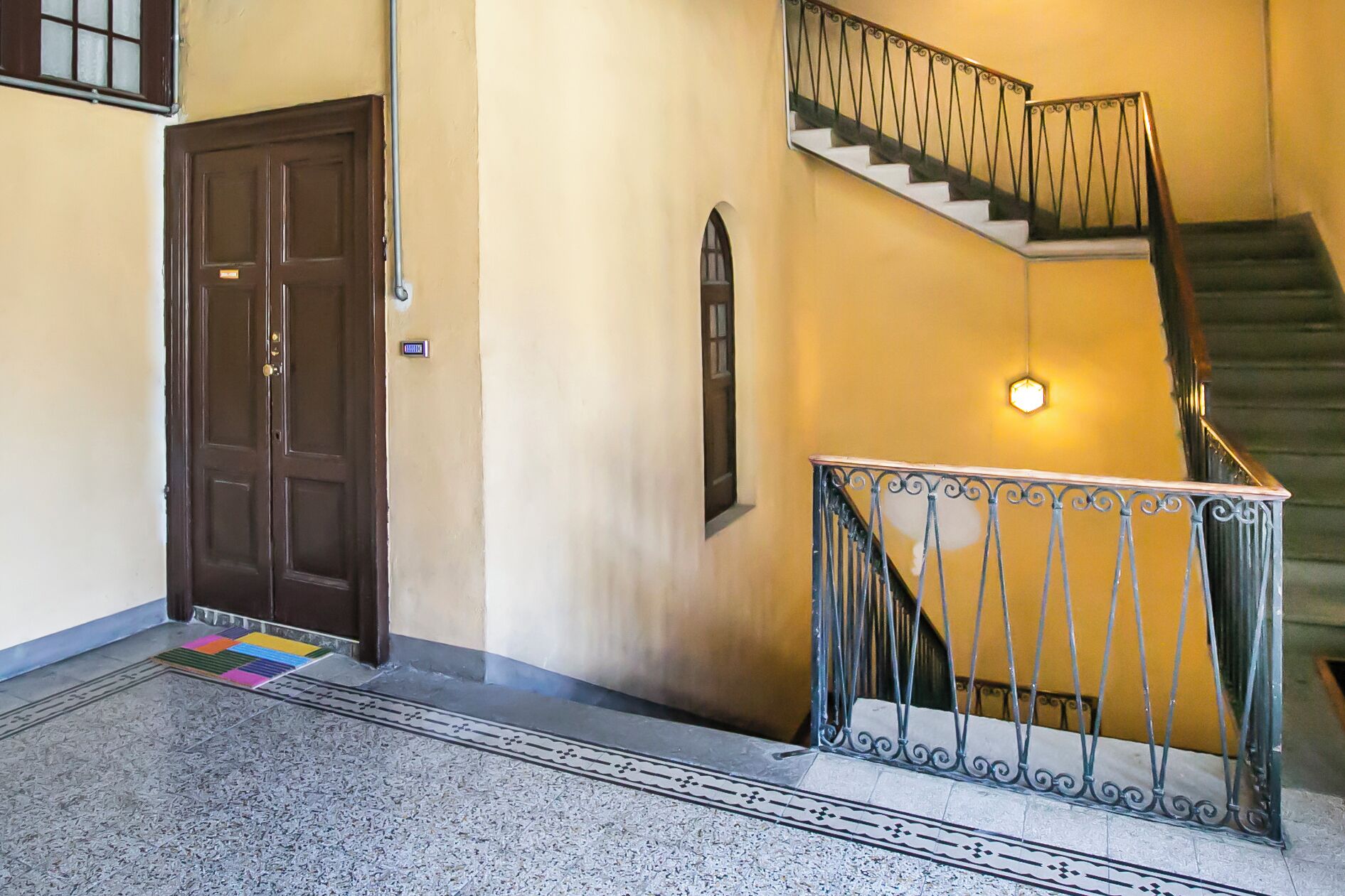 A hallway with a brown door, a small window, and a staircase with a metal railing.