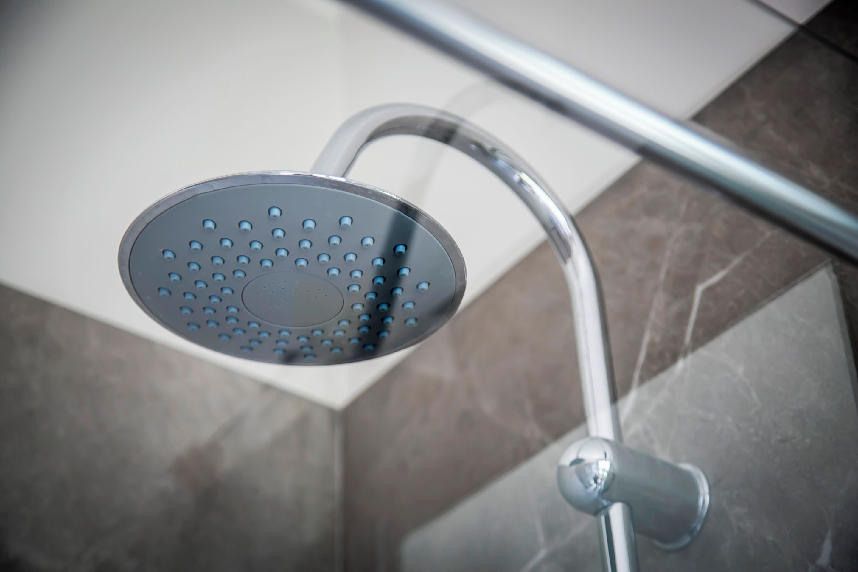 Un cabezal de ducha con un mando curvo y una perilla de control, instalado en una pared con suelo de baldosas.