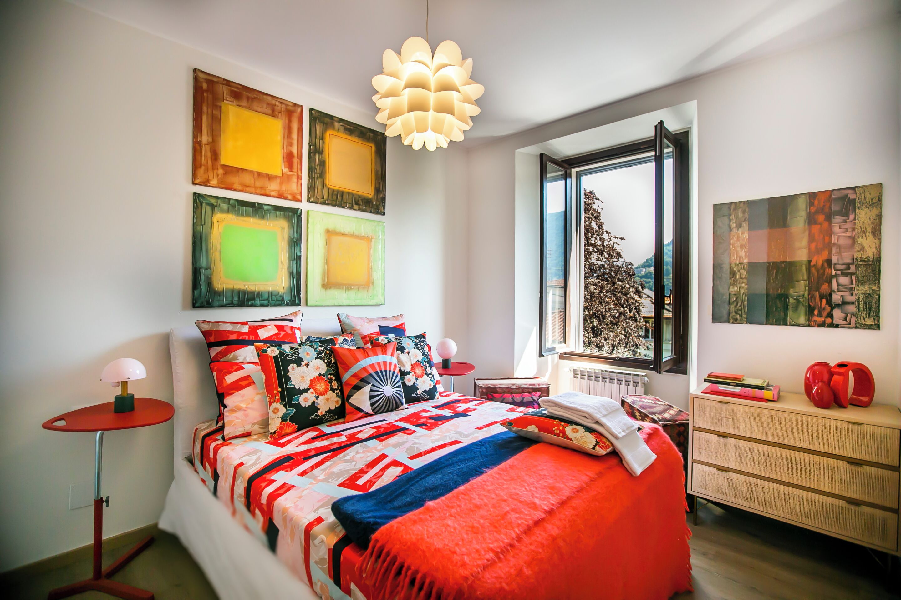 A modern bedroom with a large bed, a red lamp, and artwork on the walls.