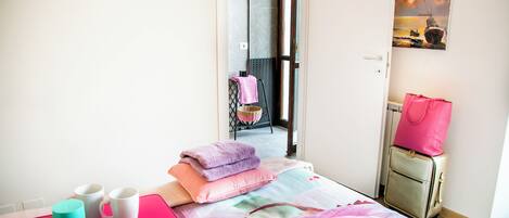Una habitación de hotel con una cama, una bandeja rosa con tazas, una maleta y un cuadro en la pared.