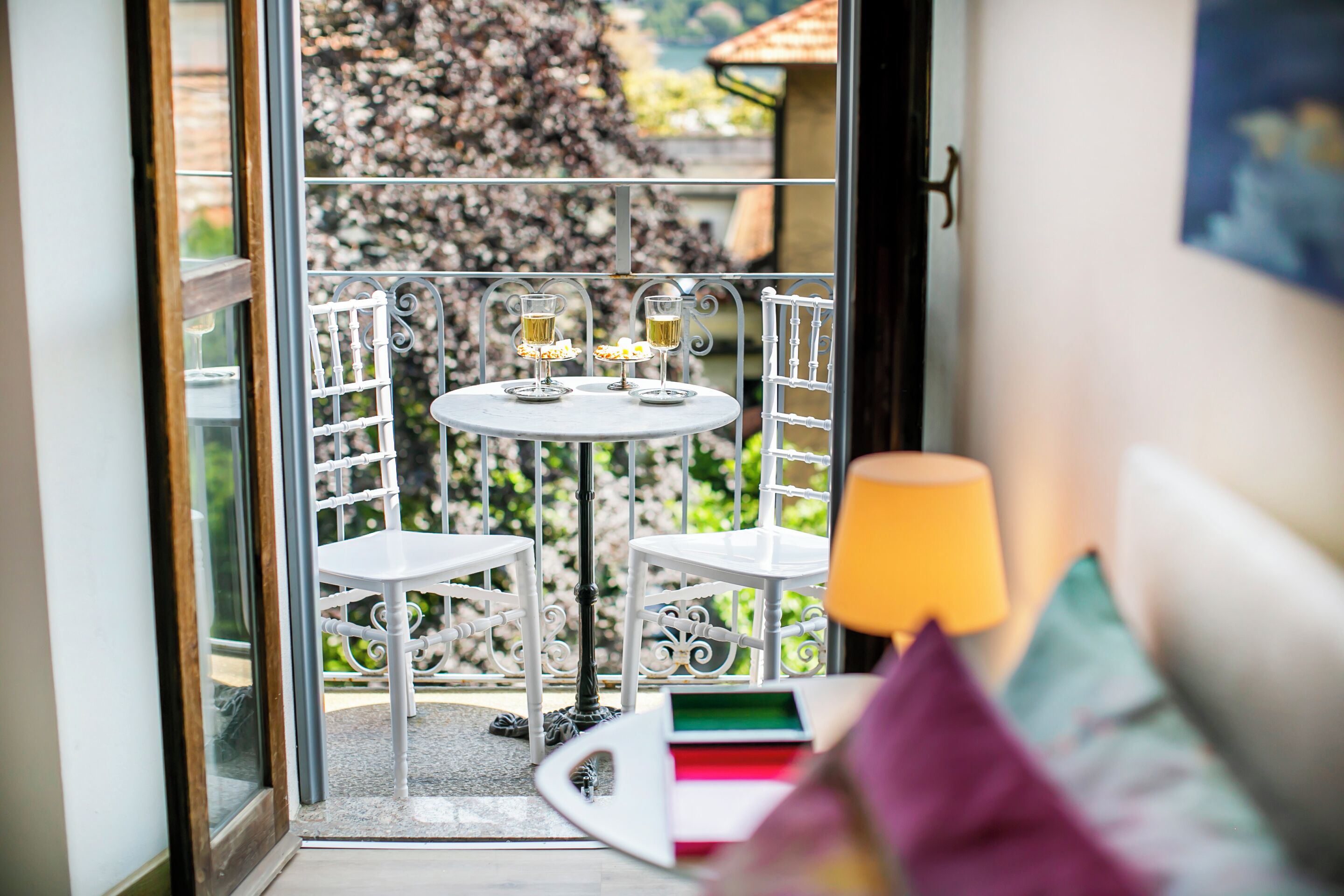 Un balcon avec une table et des chaises, deux verres de vin et une lampe.