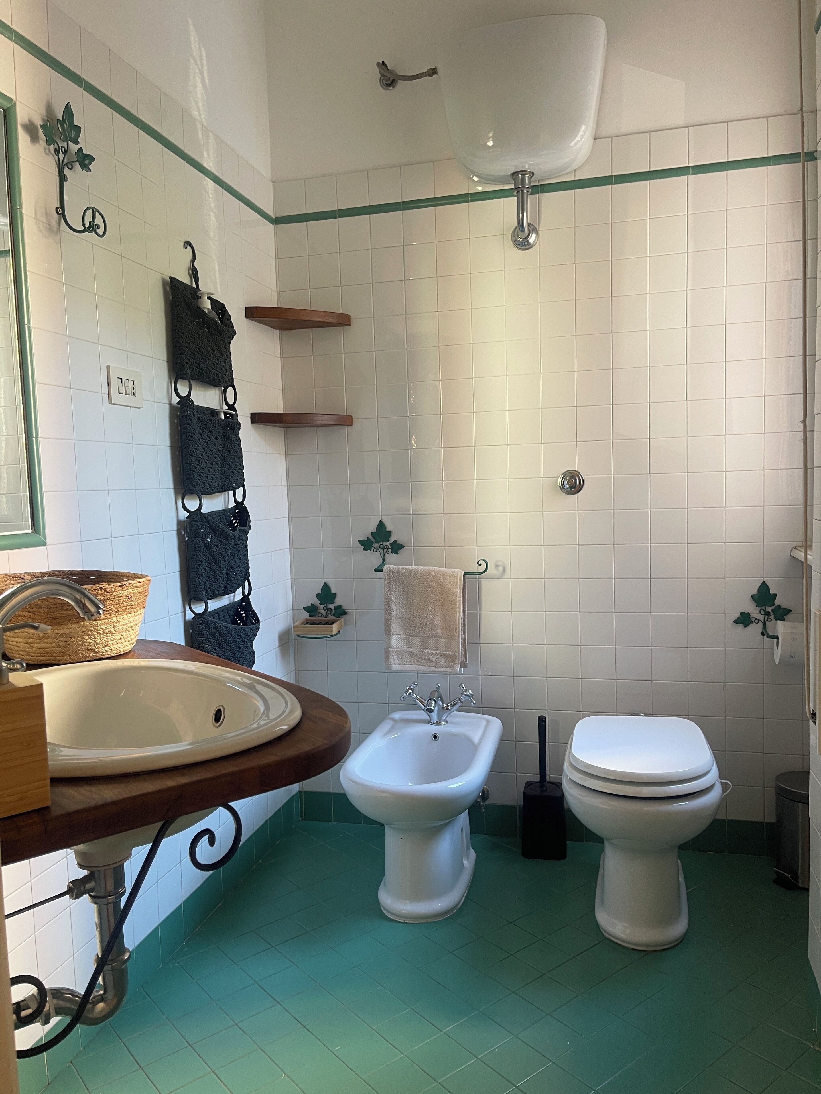 A bathroom with a white sink, bidet, and toilet, green floor tiles, and white tiled walls.