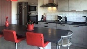 A modern kitchen with a central island, red chairs, and pendant lights.