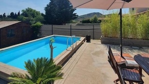A backyard with a swimming pool, a wooden deck, and a patio umbrella.