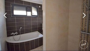 A bathroom with a bathtub, a shower, and a window above the bathtub.