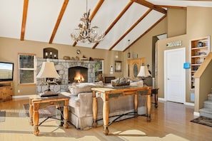 A living room with a stone fireplace, wooden furniture, a chandelier, and a staircase.