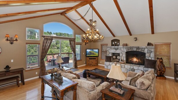A spacious living room with a stone fireplace, wooden beams, a large TV, and a cozy seating area. - Large Retreat, Arcade, Lake Access + AC (Lake Arrowhead)