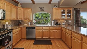 A kitchen with wooden cabinets, granite countertops, a dishwasher, and a window with a view of greenery. - Large Retreat, Arcade, Lake Access + AC (Lake Arrowhead)