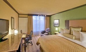 A hotel room with a bed, desk, chair, and a TV.