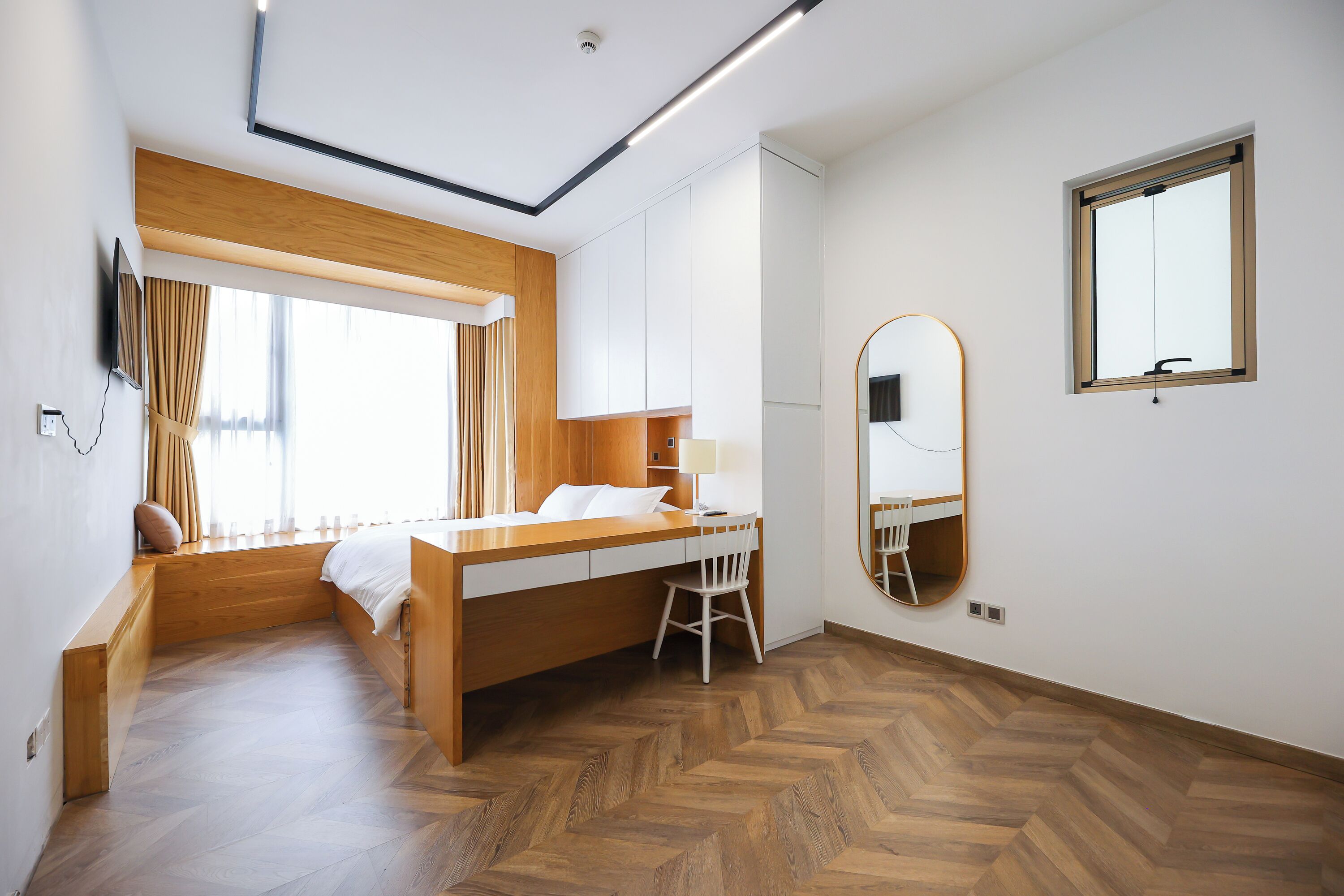 Habitación de hotel con cama, escritorio, silla y un espejo grande.