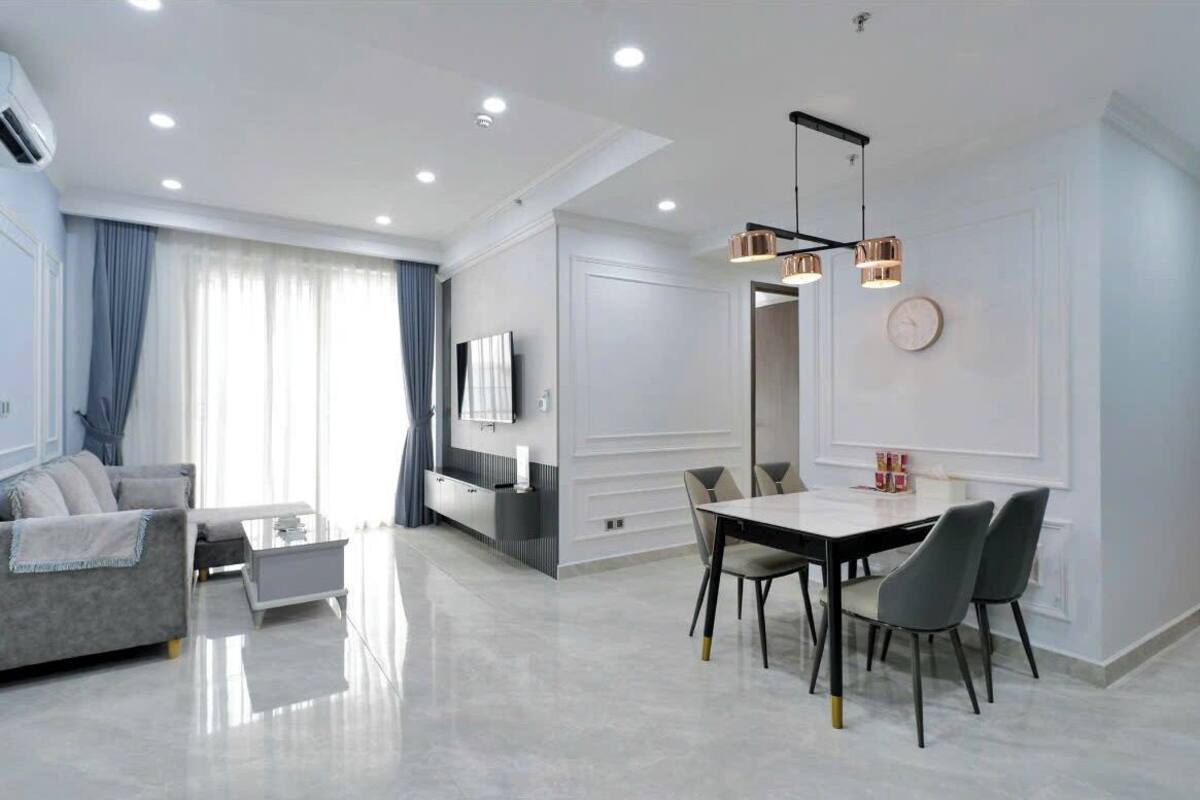 Uma sala de estar moderna com um sofá cinzento, uma mesa de centro e uma TV. Há também um espaço de refeições com uma mesa e cadeiras.