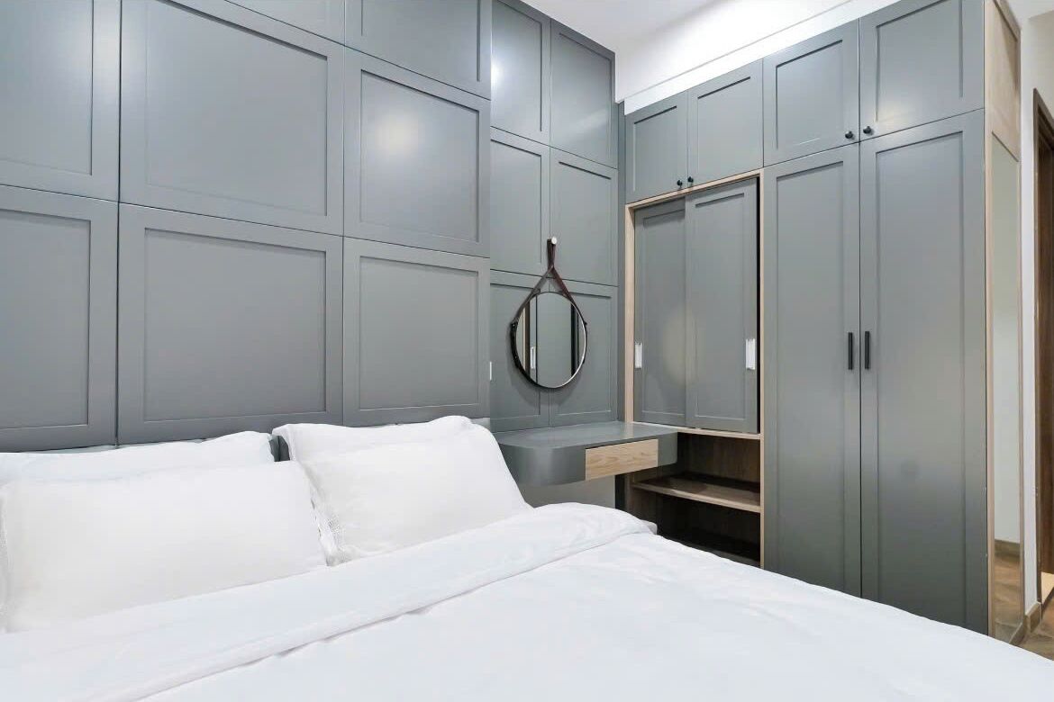 Quarto com cama, guarda-roupa cinzento e espelho.