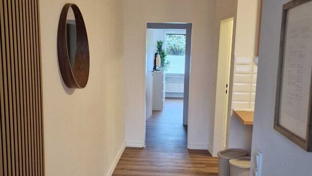 Un pasillo con piso de madera, pared de listones de madera y un espejo circular.