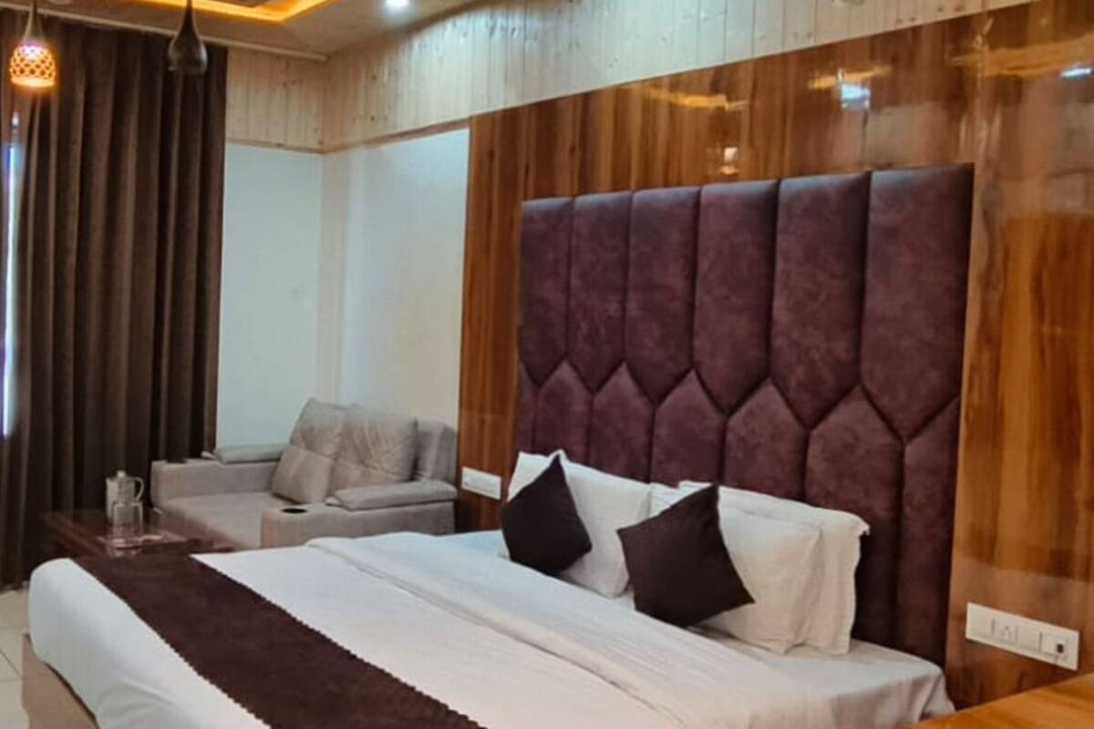 Habitación de hotel con una cama grande, un sofá, un cabecero de madera y una ventana con cortinas.