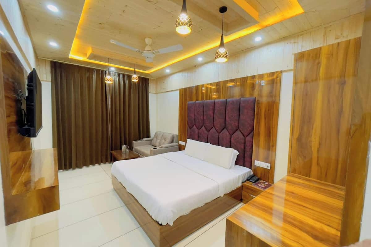 Un dormitorio moderno con una cama grande, un cabecero de madera, una mesita de noche, una zona de estar con un sofá y un televisor montado en la pared.
