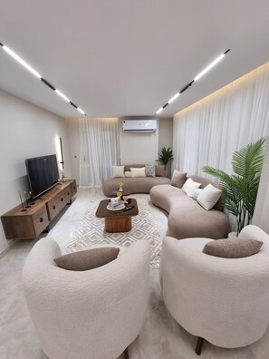 Una sala de estar moderna con un sofá, una mesa de centro, un televisor sobre un mueble de madera y una planta en maceta.