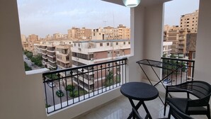 Un balcon donnant sur un quartier résidentiel, avec une rambarde en métal et une table entourée de chaises.