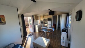 A compact kitchen with a dining area, a refrigerator, and a microwave. - Mobil chalet (Blars)